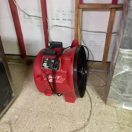 Red air mover drying a room where the lower wall was opened and plastic sheeting hangs nearby