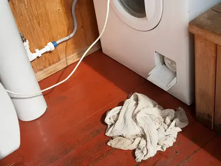 A washing machine supply hose leaking onto a wood laundry room floor